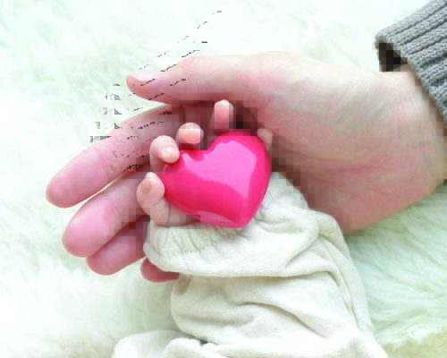 Baby's hand with heart object and mother's hand