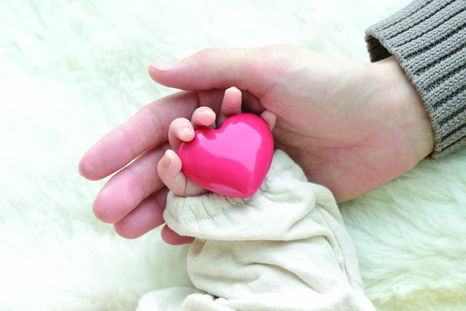 Baby's hand with heart object and mother's hand